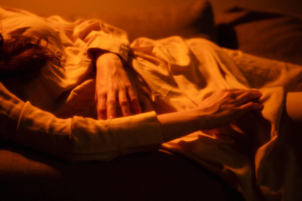 Pessoa relaxando no quarto ao anoitecer, preparando-se para sua rotina noturna com uma xícara de chá e um livro